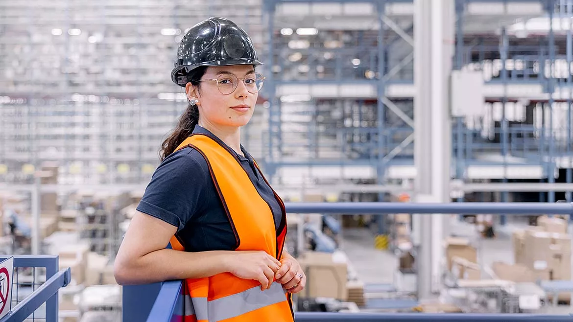 Warehouse Safety and Logistics Operations Management Worker wearing a safety vest and hard hat in a warehouse.