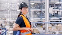 Worker wearing a safety vest and hard hat in a warehouse.