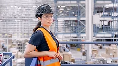 Worker wearing a safety vest and hard hat in a warehouse.
