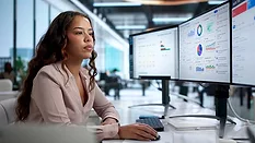 Data Analytics and Quality Management Dashboard Monitoring Person reviewing analytics dashboards on multiple computer monitors.