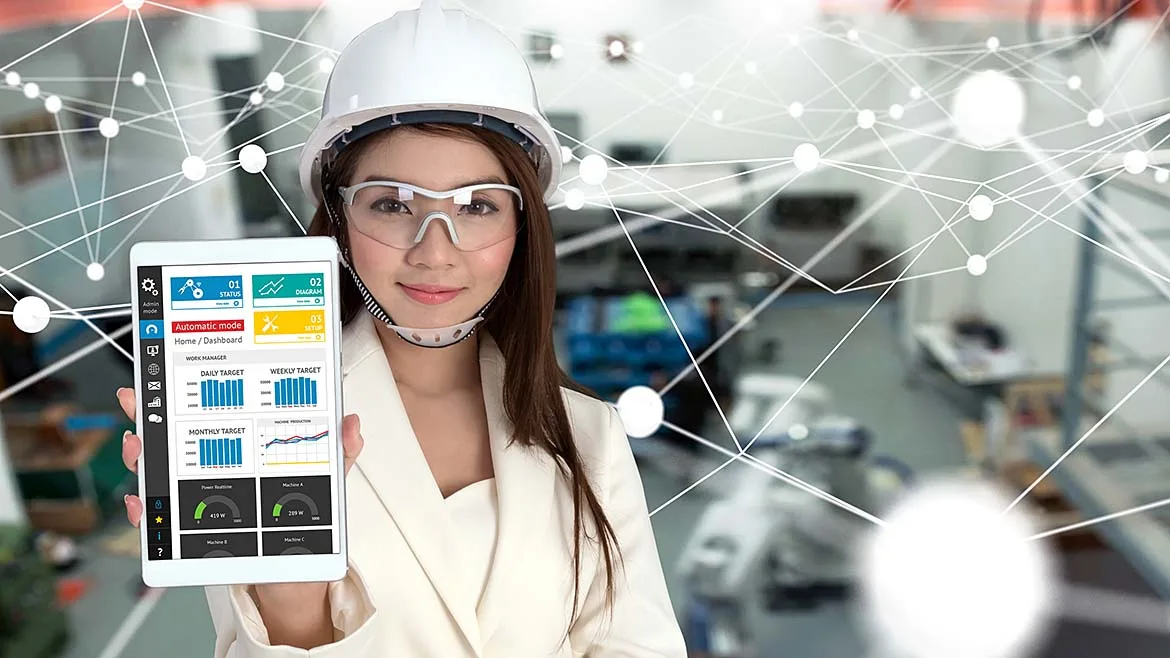 Engineer wearing safety glasses and a hard hat displaying a factory analytics dashboard on a tablet, illustrating connected manufacturing and industrial IoT technologies.