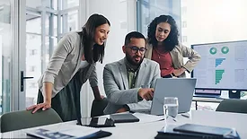Business professionals reviewing analytics and performance data on a laptop and dashboard display during a team collaboration meeting.