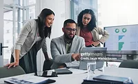 Business professionals reviewing analytics and performance data on a laptop and dashboard display during a team collaboration meeting.