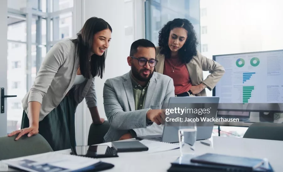 Business professionals reviewing analytics and performance data on a laptop and dashboard display during a team collaboration meeting.