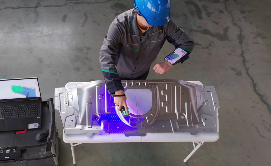 Technician using a handheld 3D scanner to inspect a metal automotive component, capturing dimensional data for quality control and manufacturing verification.