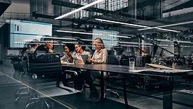 Business professionals collaborating in a modern conference room, reviewing data and discussing strategy using tablets and digital dashboards.