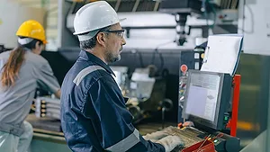CNC operator monitoring a machining center control panel.