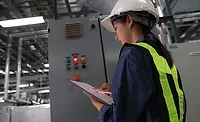 Industrial Maintenance Inspection Industrial worker wearing a hard hat and high-visibility vest inspecting equipment and reviewing maintenance data on a tablet in a manufacturing facility.