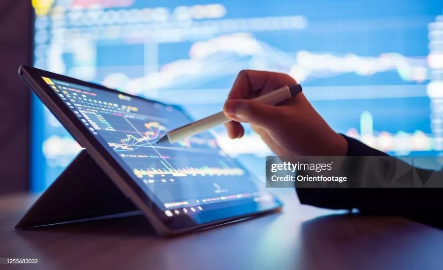 Hand using a stylus on a tablet displaying manufacturing data analytics, performance charts, and production metrics for real-time industrial decision-making.