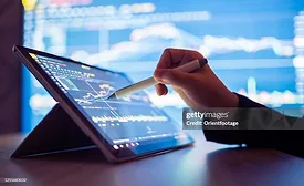 Hand using a stylus on a tablet displaying manufacturing data analytics, performance charts, and production metrics for real-time industrial decision-making.