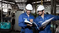 Manufacturing Engineers Reviewing Production Plans Two manufacturing engineers reviewing production plans on a factory floor.