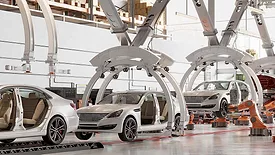 Automated automotive assembly line with robotic systems and vehicle bodies moving through a modern car manufacturing facility.
