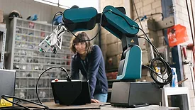 Collaborative robot equipped with a precision tool operating in a manufacturing workspace while an engineer monitors the robotic system in the background.