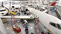 Aircraft maintenance hangar with multiple business jets undergoing inspection, repair, and maintenance, supported by technicians, tools, and service equipment.