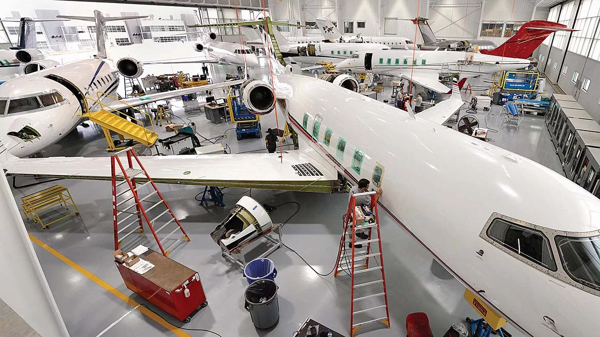 Aircraft maintenance hangar with multiple business jets undergoing inspection, repair, and maintenance, supported by technicians, tools, and service equipment.