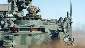 Soldier giving a thumbs-up from the hatch of an armored military vehicle.