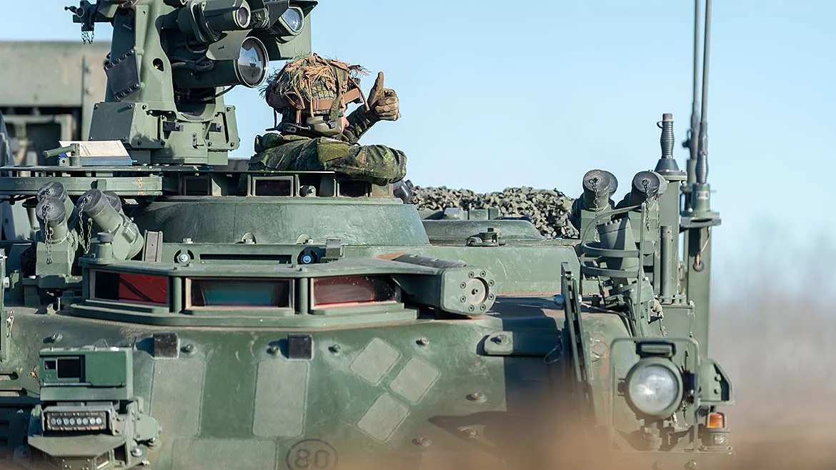 Soldier giving a thumbs-up from the hatch of an armored military vehicle.
