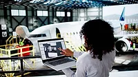 Aerospace Engineer Reviewing Digital Twin Model Aerospace engineer reviewing a digital twin model on a laptop beside an aircraft.