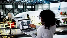 Aerospace engineer reviewing a digital twin model on a laptop beside an aircraft.