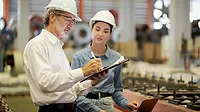 Two quality auditors reviewing production records on a factory floor.