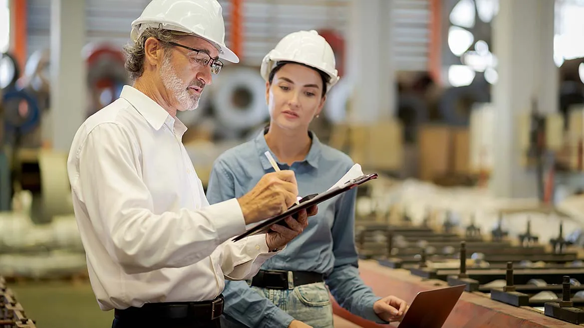 Quality Auditors Reviewing Manufacturing Operations Two quality auditors reviewing production records on a factory floor.
