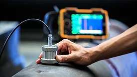 Technician performing ultrasonic testing on a metal pipe with a handheld probe.