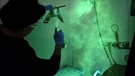 Technician performing fluorescent penetrant inspection on a metal component under UV light.