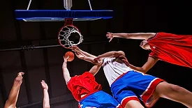 Basketball players reaching for the ball beneath the hoop during a game.
