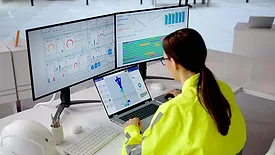 Engineer monitoring digital manufacturing dashboards and a 3D part model on multiple displays.