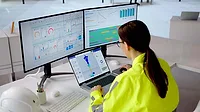 Engineer Monitoring Digital Manufacturing Dashboard Engineer monitoring digital manufacturing dashboards and a 3D part model on multiple displays.