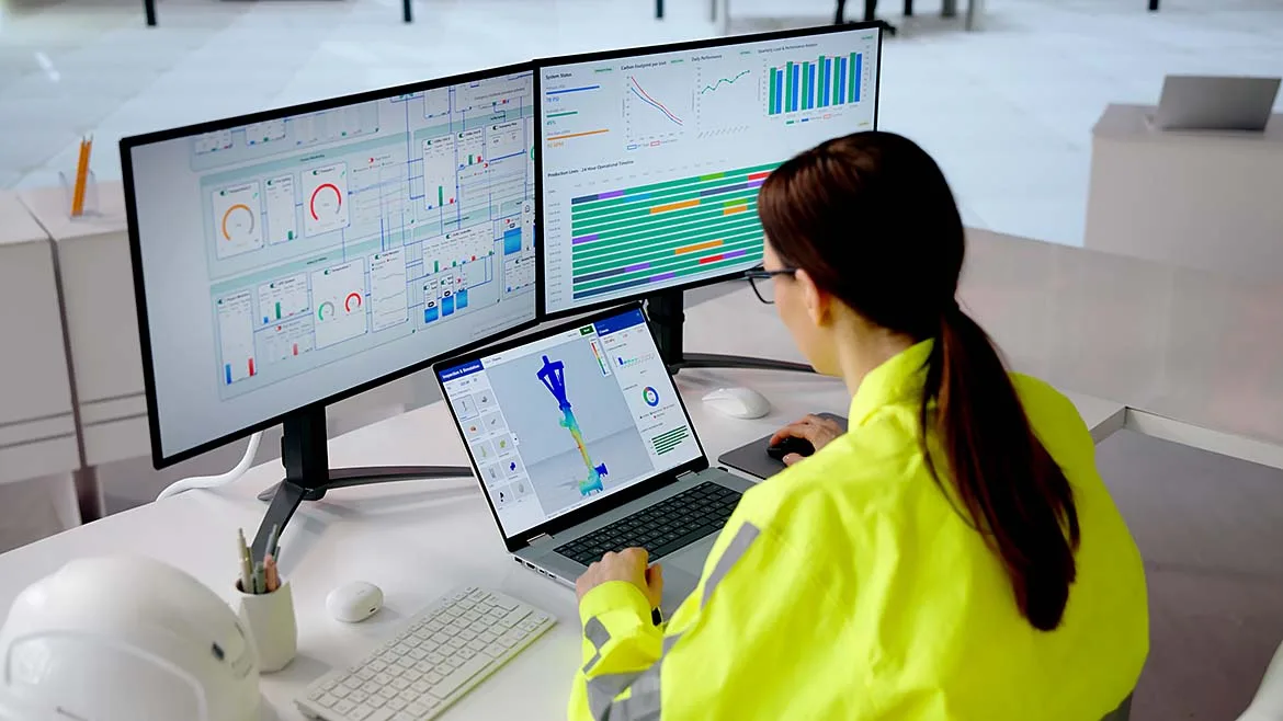 Engineer monitoring digital manufacturing dashboards and a 3D part model on multiple displays.