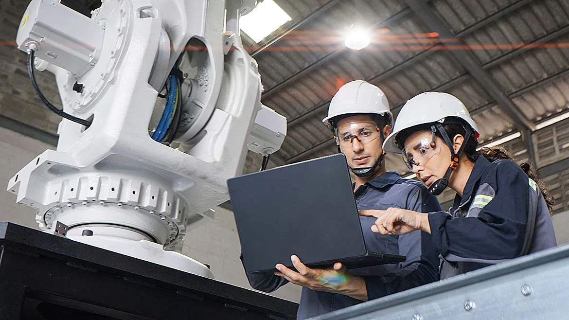 Two engineers reviewing robotic system data beside an industrial robot.