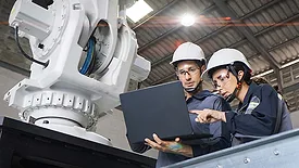 Two engineers reviewing robotic system data beside an industrial robot.
