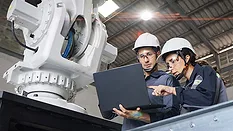 Engineers Reviewing Industrial Robot Performance Two engineers reviewing robotic system data beside an industrial robot.