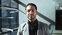 Professional portrait of a man wearing glasses and a gray blazer.