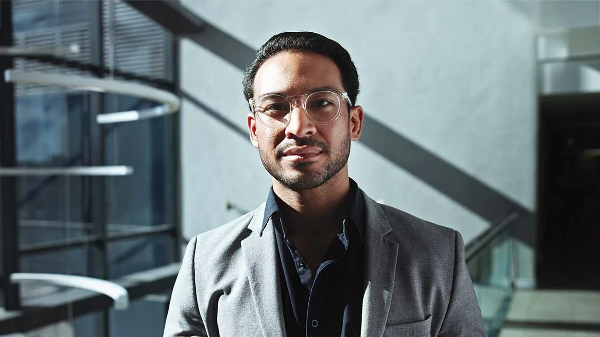 Professional portrait of a man wearing glasses and a gray blazer.