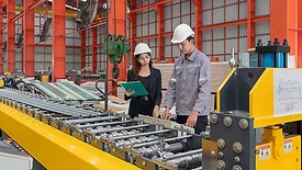 Two manufacturing professionals reviewing production equipment on a factory floor.