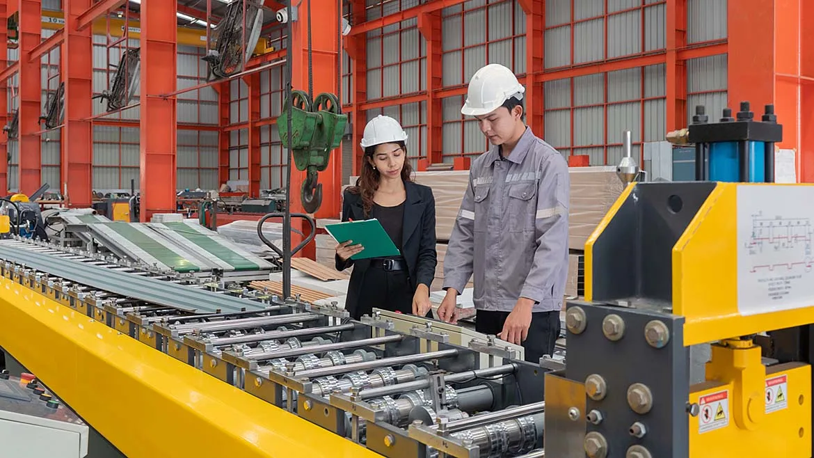 Two manufacturing professionals reviewing production equipment on a factory floor.