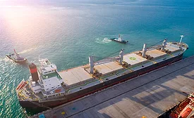 Aerial view of general bulk cargo ship vessel on departure unberthing from the sea port terminal, assisted by a tug boat.