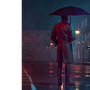 Man with umbrella and coat stands outside while it rains at night looking at a building.