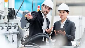 Senior official woman and male architectural engineer talking, wearing suits and safety hats.