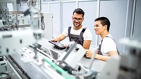 Young quality professionals servicing modern industrial manufacturing machine in production factory.