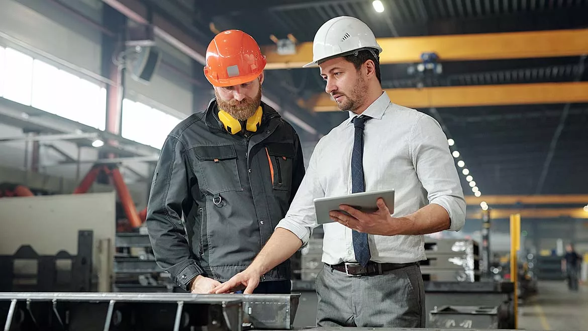 Two workers in hard hats examining produced metal parts.