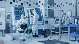Sterile Modern Factory: Professionals in Coveralls, Masks Working on CNC Machinery. Medical Electronics Manufacturing Laboratory with High Tech Robot Arm Production Line and Contemporary Equipment.