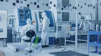 Sterile Modern Factory: Professionals in Coveralls, Masks Working on CNC Machinery. Medical Electronics Manufacturing Laboratory with High Tech Robot Arm Production Line and Contemporary Equipment.