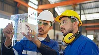 Engineer wearing safety helmet and glasses, explaining the project diagram using a futuristic tablet, with a manager in the manufacturing factory.