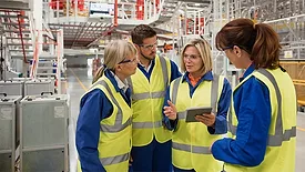 QM 0124 Fellow Traveler Column. Factory workers on the manufacturing floor having a discussion.