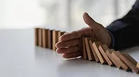 A hand blocks falling dominoes A hand prevents wooden blocks from falling