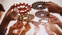 People's hands joining different metal cog wheel together. People's hands joining different metal cog wheel together.