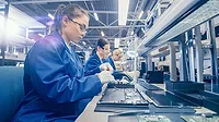 High Tech Factory Facility with Three Female Factory Workers Women electronics factory workers in blue work coat and protective glasses are assembling laptop motherboards with a screwdriver.